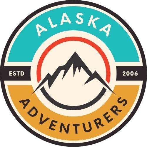 This is the round logo for this website. It is outlined in black and the inside colors are turquoise, yellow-orange, and white, with a red and black line. It says Alaska Adventurers, ESTD 2006. There is an outline of a mountain in black in the center.